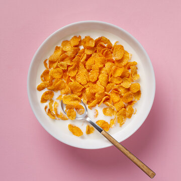 Top view of cornflakes in a bowl with milk on a pink background