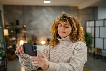 smiling adult woman take a self portrait with mobile phone at home