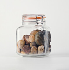 A clear glass jar with an orange seal containing multicolored smooth pebbles, neatly arranged, showcasing a simple yet elegant arrangement perfect for home decor enthusiasts.