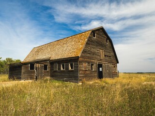 Rustic wooden barn set in a vast field under a blue sky, capturing rural charm and simplicity.