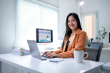 A woman is sitting at a desk with a laptop and a cup of coffee