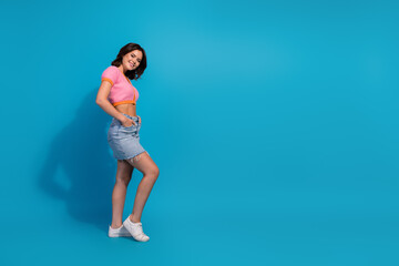 Trendy young woman wearing casual stylish outfit on blue background, smiling confidently, standing in relaxed pose