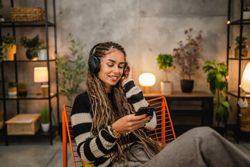 young woman with headphones use mobile phone and enjoy on armchair