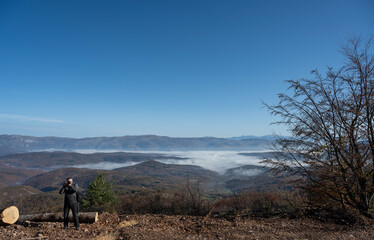 Obraz premium A nature photographer takes a photo of a mountain range that is partially covered in fog, with a beautiful clear blue sky above. A beautiful nature photo.