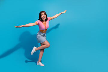 Obraz premium Joyful young woman playfully posing against a vibrant blue background showcasing casual fashion and summer style