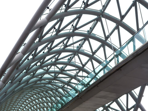 Scene of modern construction of arch ceiling over the glass pathway, bridge of peace, Tbilisi architecture in Georgia. Curved structure supporting roof in building, curvature line background.