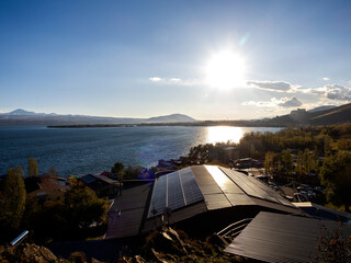 Solar panels on home rooftop in village near the beautiful lake with sun on blue sky background....