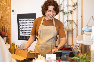 Smiling employee packaging a organic product at a shop shop counter