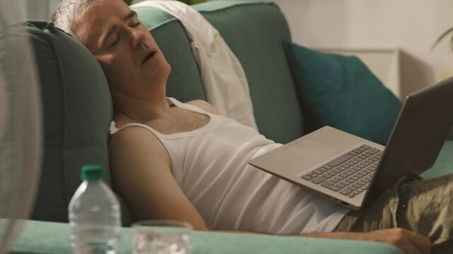 Exhausted man falling asleep on the couch during the summer heatwave