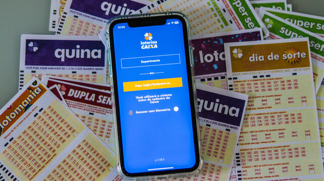 Celular exibindo o aplicativo Loterias Caixa, com cartelas de loteria vis&iacute;veis ao fundo, destacando a interface de apostas e sorteios. S&atilde;o Paulo SP em 10 Jan 25