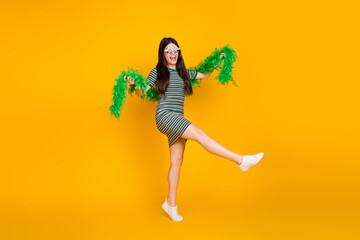 Young Woman in Striped Dress Dancing Playfully Holding Green Boa Against Yellow Background