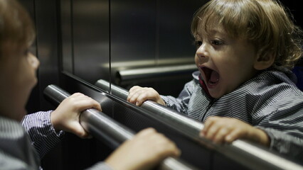 Cute baby toddler playing inside elevator staring at mirror reflection