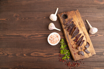 Armenian Basturma dried meat on wooden cutting board with pepper and herbs on brown wooden. Top...