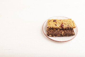 granola bars with caramel, nuts, flakes in ceramic plate on white wooden. Side view, copy space.