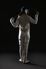 Fencer with epee on dark background, back view