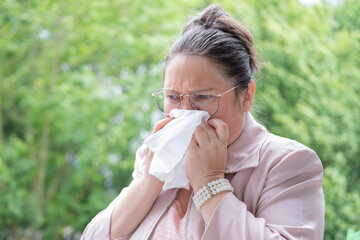 middle-aged businesswoman uses tissue to blow nose, indicating health issues, immune system,...