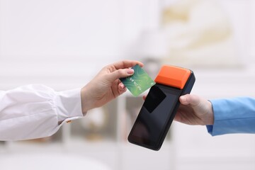 Woman paying with credit card via terminal against blurred background, closeup