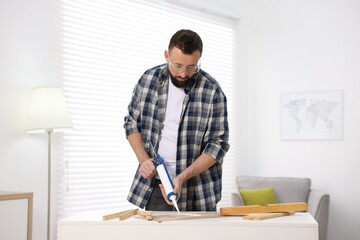 Man with caulking gun glueing plywood indoors