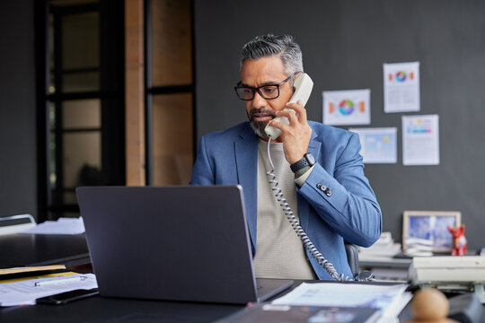 Mature indian businessman on call while working on laptop