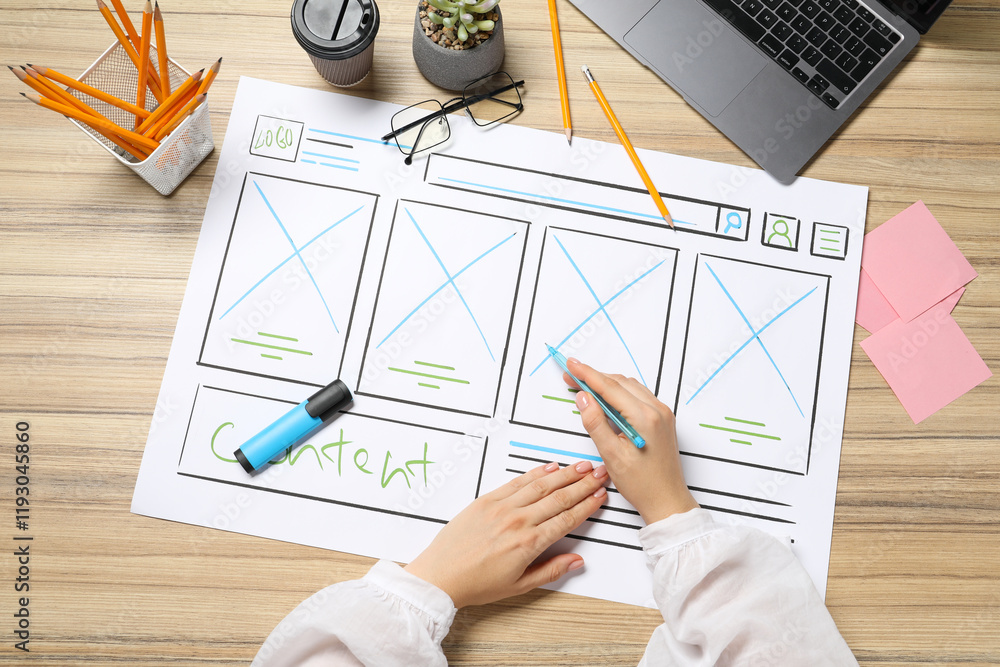 Poster website designer creating wireframe on paper with pen at wooden table, top view
