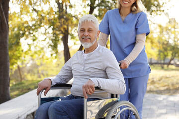 Caregiver assisting senior man on wheelchair in park. Home health care service