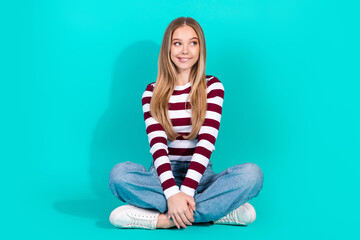 Portrait of a young woman with a casual and trendy outfit sitting against a teal background