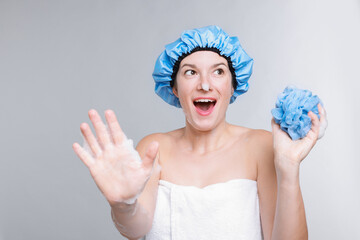 Emotional woman with shower cap and mesh sponge making stop gesture on grey background