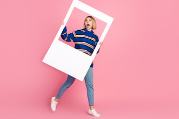 Young woman holding a photo frame in excitement against pink background