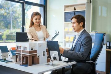 A businessman and woman sit at a table, discussing a two-story house for sale in a village project. They focus on property details, real estate opportunities, and housing investments