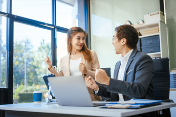 A businessman and woman sit at a modern office table, smiling and discussing a new project or business startup. They collaborate with a laptop, focusing on strategic planning and teamwork
