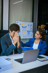 A stressed businessman and woman sit at a desk, overwhelmed by business challenges. They discuss problems,financial pressures, and strategy, seeking solutions to manage work, deadlines, and economic
