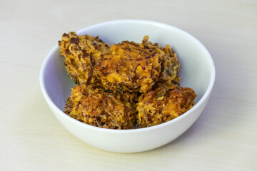 A bowl of crispy pakora, served on a white bowl. These delectable deep-fried fritters are a beloved snack or appetizer throughout Bangladesh, India, and other regions of South Asia.