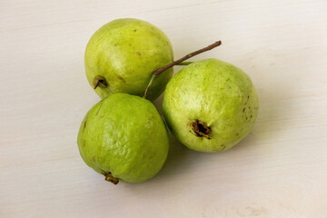 Three fresh ripe guavas are displayed on a wooden surface.