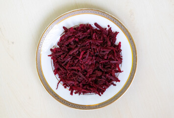 Thinly sliced or grated beetroot fritters are presented on a white ceramic plate against a light wooden backdrop. Perfect for a healthy diet. Top view.