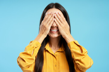Happy Latin woman covering eyes and smiling on blue background