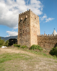 Historic stone tower at a medieval fortress surrounded by greenery and mountains on a clear sunny day