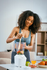 An African American woman in sportswear sits on a sofa near the dining table, preparing a healthy...