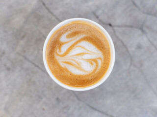 A paper cup of cappuccino coffee is placed on a cement table, with a flat lay shot. Coffee latte art.