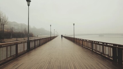 Fototapeta premium Solitary figure walking on a foggy boardwalk by a river.