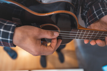 Close-up perspective captures a man's fingers plucking the strings of a glossy black ukulele....