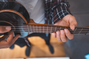 Fototapeta premium Close-up perspective captures a man's fingers plucking the strings of a glossy black ukulele. Making a music. Pleasure of playing an instrument