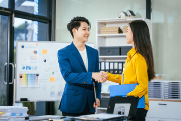 A businessman and businesswoman shake hands during a meeting at the office,signifying...
