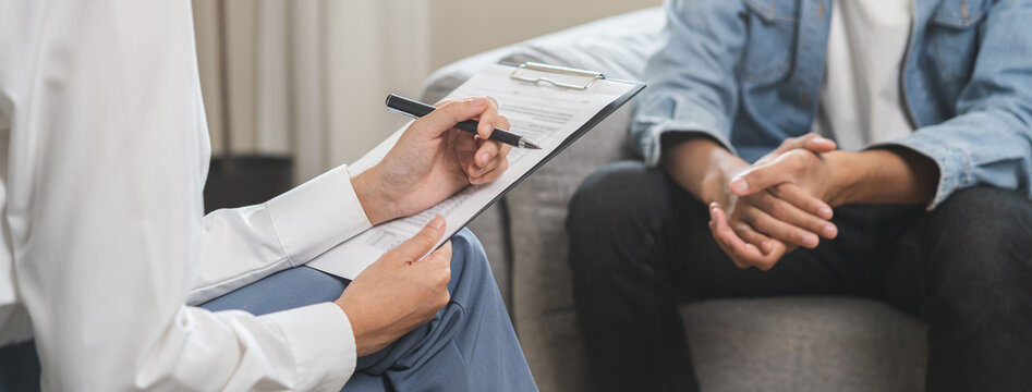 Psychology, depression. Happy smile asian young man patient mental therapy explain symptom with psychologist while doctor woman taking notes at clinic. Psychologist with sick mental health person.