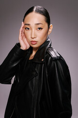 Asian woman in black leather jacket posing with hand on head fashionable and stylish look for a...