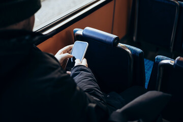 A man is riding public transport and using a smartphone, close up.