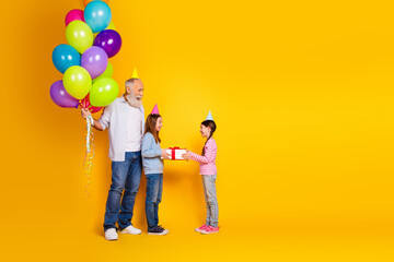 Fototapeta premium Grandfather and granddaughters celebrating a birthday with balloons and gifts against a vibrant yellow background