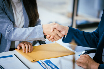 A male lawyer is shaking hands with a female client at a desk in a law office. They finalize a...