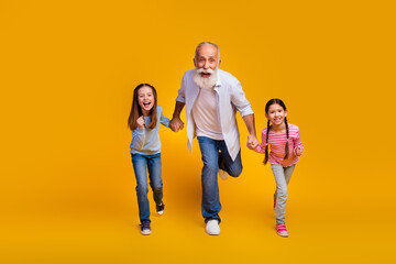 Fototapeta premium Cheerful elderly man enjoying a fun and active moment with two joyful young girls against a vibrant yellow background