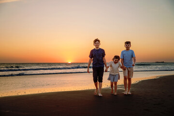 Three kids silhouettes running and jumping on beach at sunset. happy family, two school boys and one little preschool girl. Siblings having fun together. Bonding and family vacation.