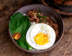 Rice bowl with black pepper roast beef and fried egg served on a wooden table.